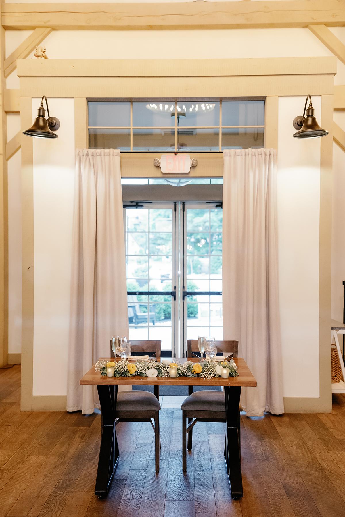 Elegant table set for two with flowers, against white curtains and wooden floor.