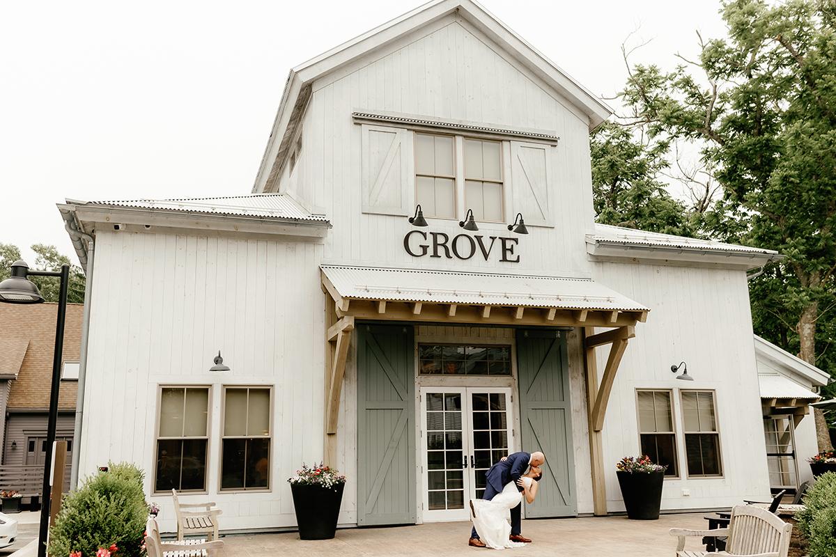 White barn-style building with "GROVE" sign, plants, and a person crouching in front.