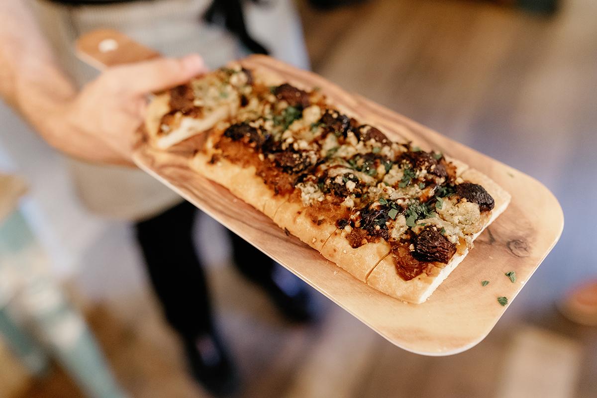 Flatbread with toppings served on a wooden tray.