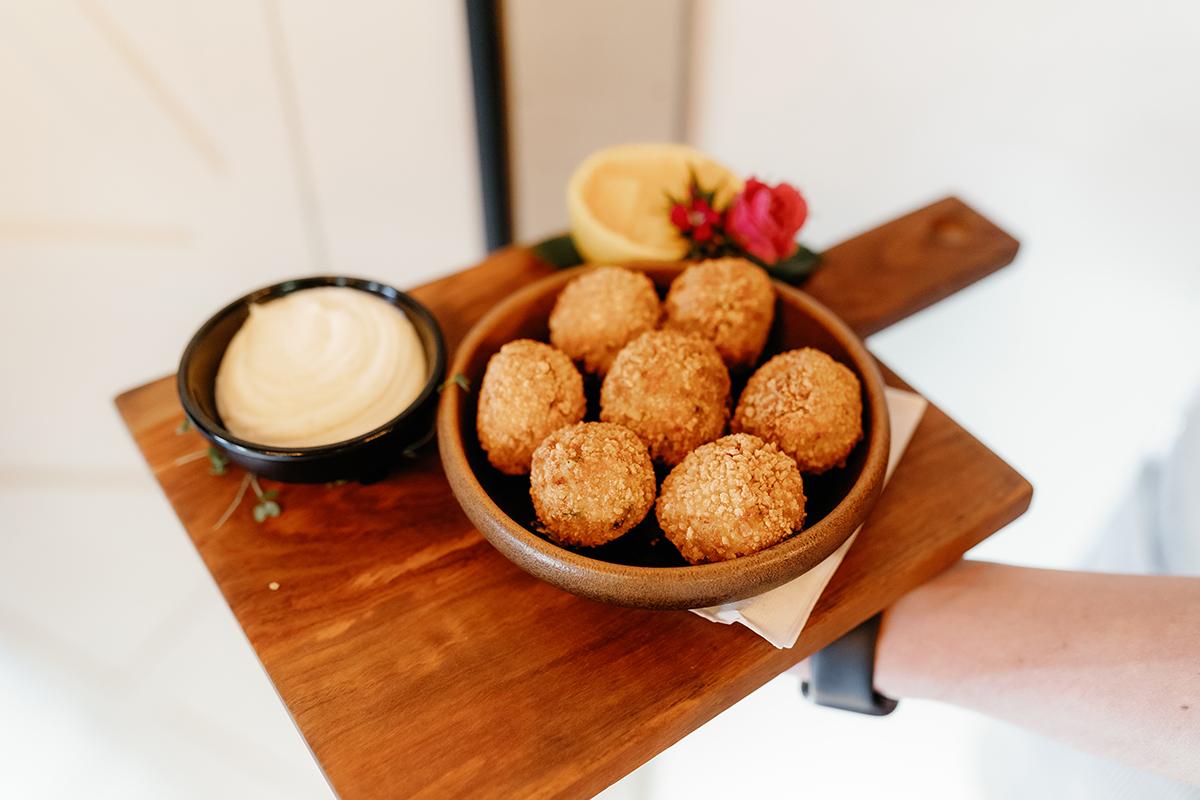 Fried balls with dips and lemon on a wooden board.