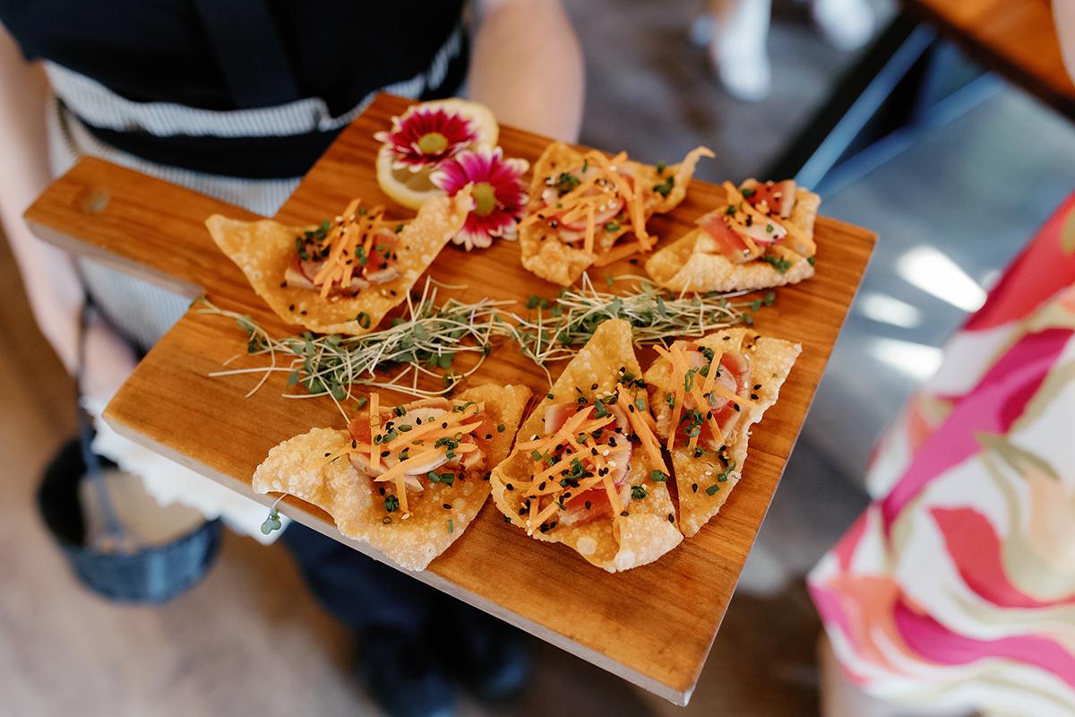 Chips topped with shredded vegetables on a wooden tray, garnished with small flowers.