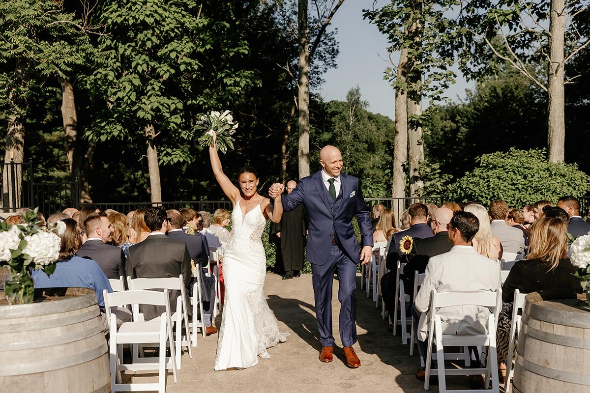 Bride and groom holding hands, celebrating outdoors among guests.