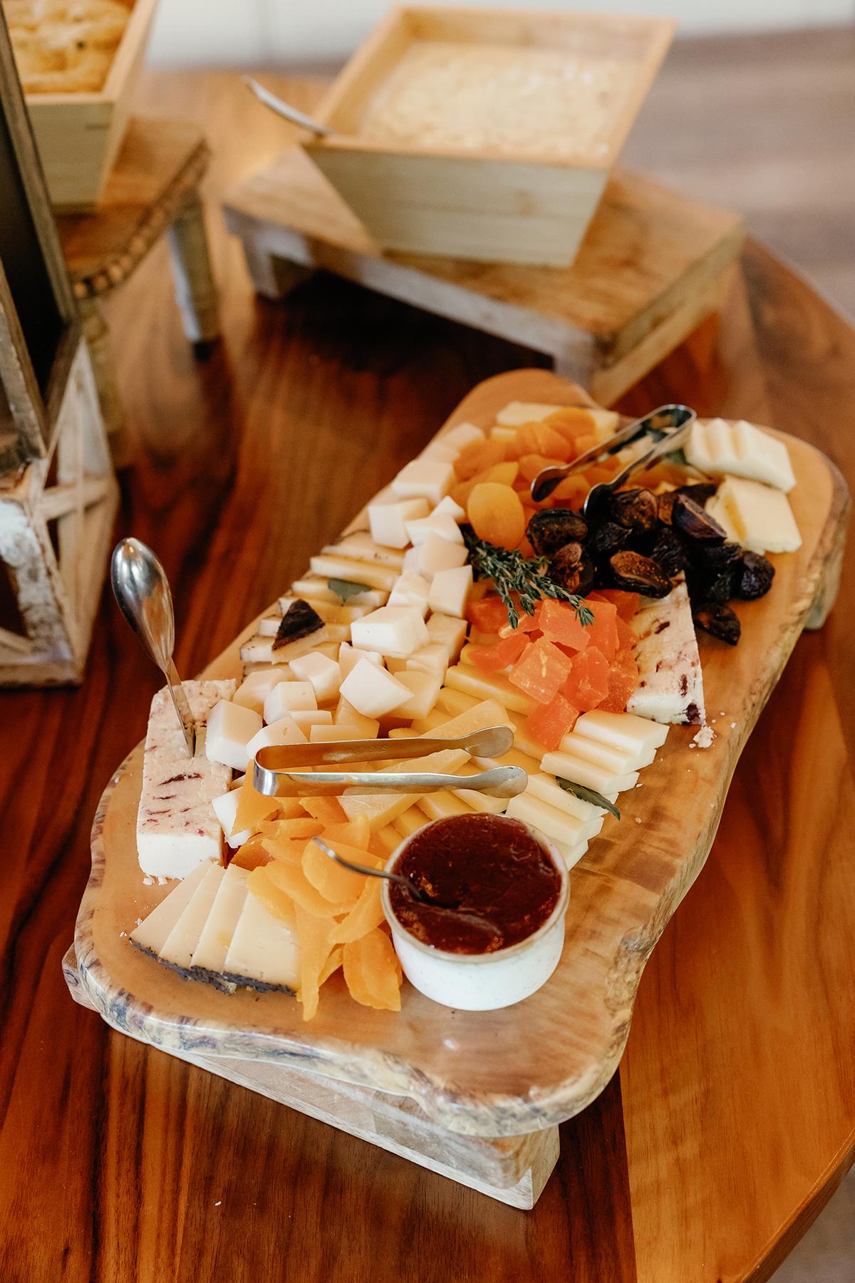 Cheese platter with assorted cheeses, nuts, and fruits on a wooden board.