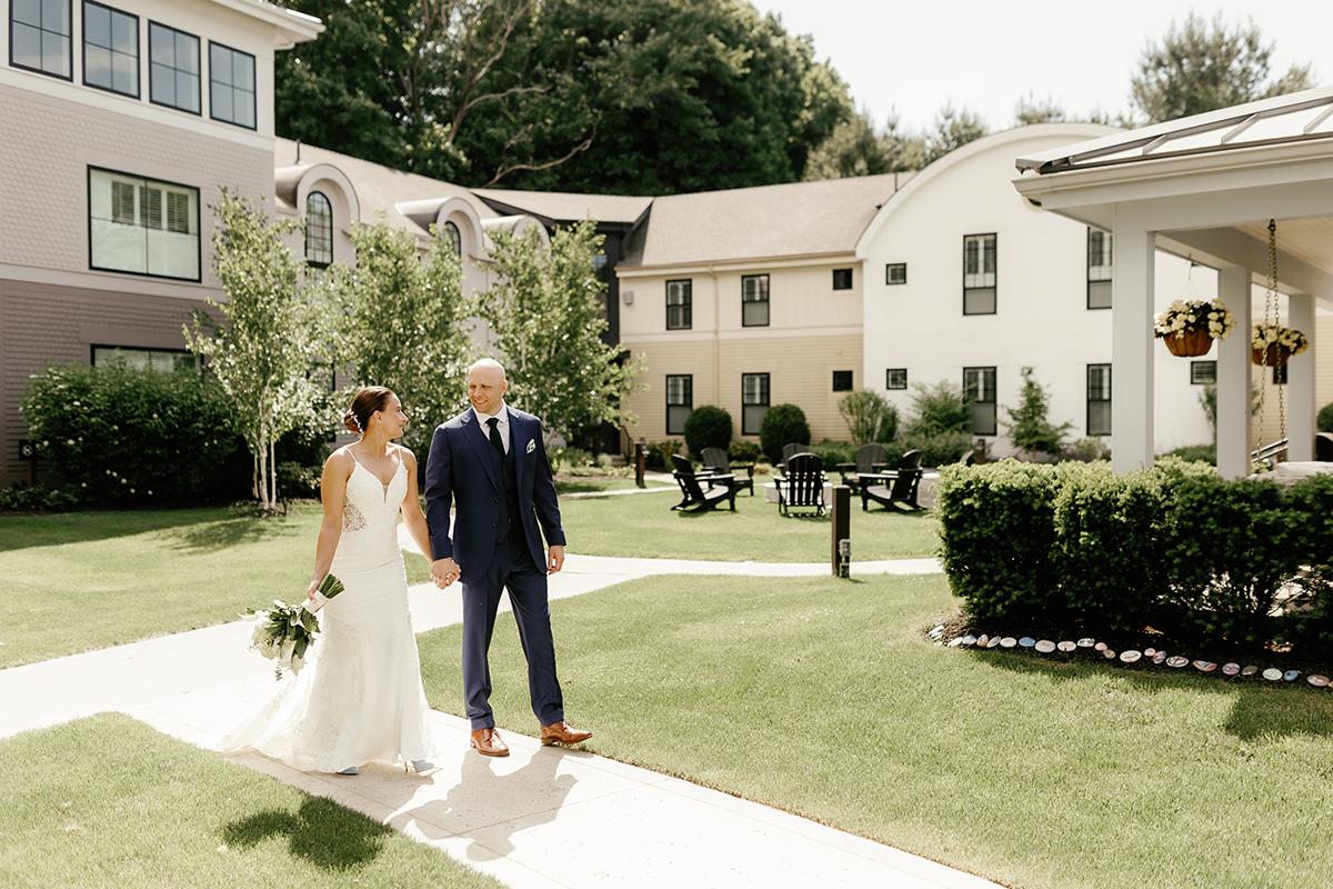 Bride and groom walking hand in hand in a sunny garden courtyard.