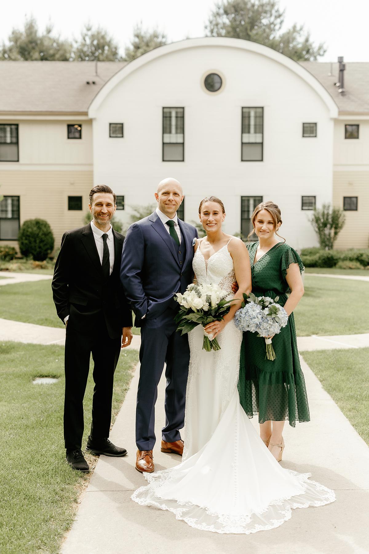 Wedding party with bride, groom, and two attendants smiling outside in a garden setting.