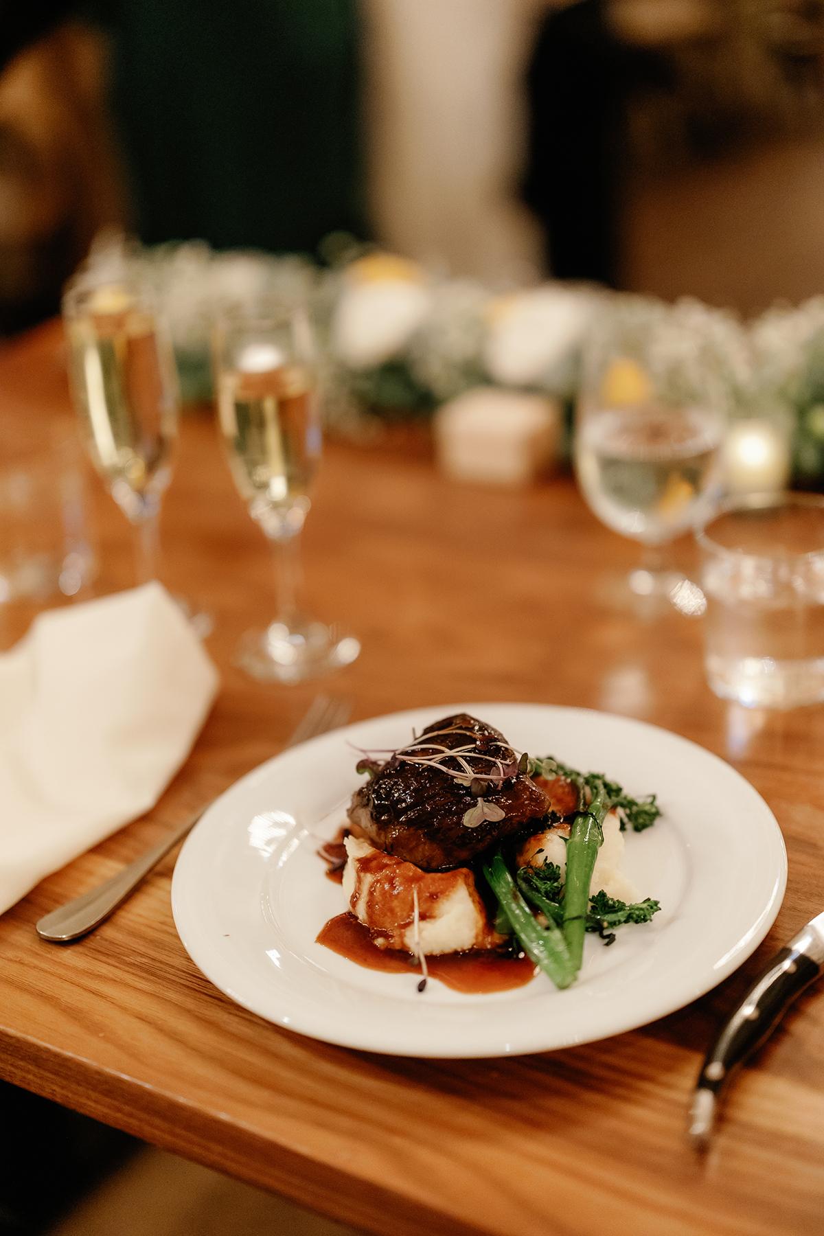Plated gourmet meal with vegetables and sauce, surrounded by wine glasses on a wooden table.