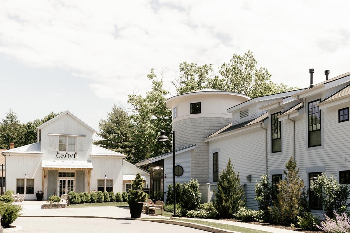 White farmhouse with silo, surrounded by trees on a sunny day.