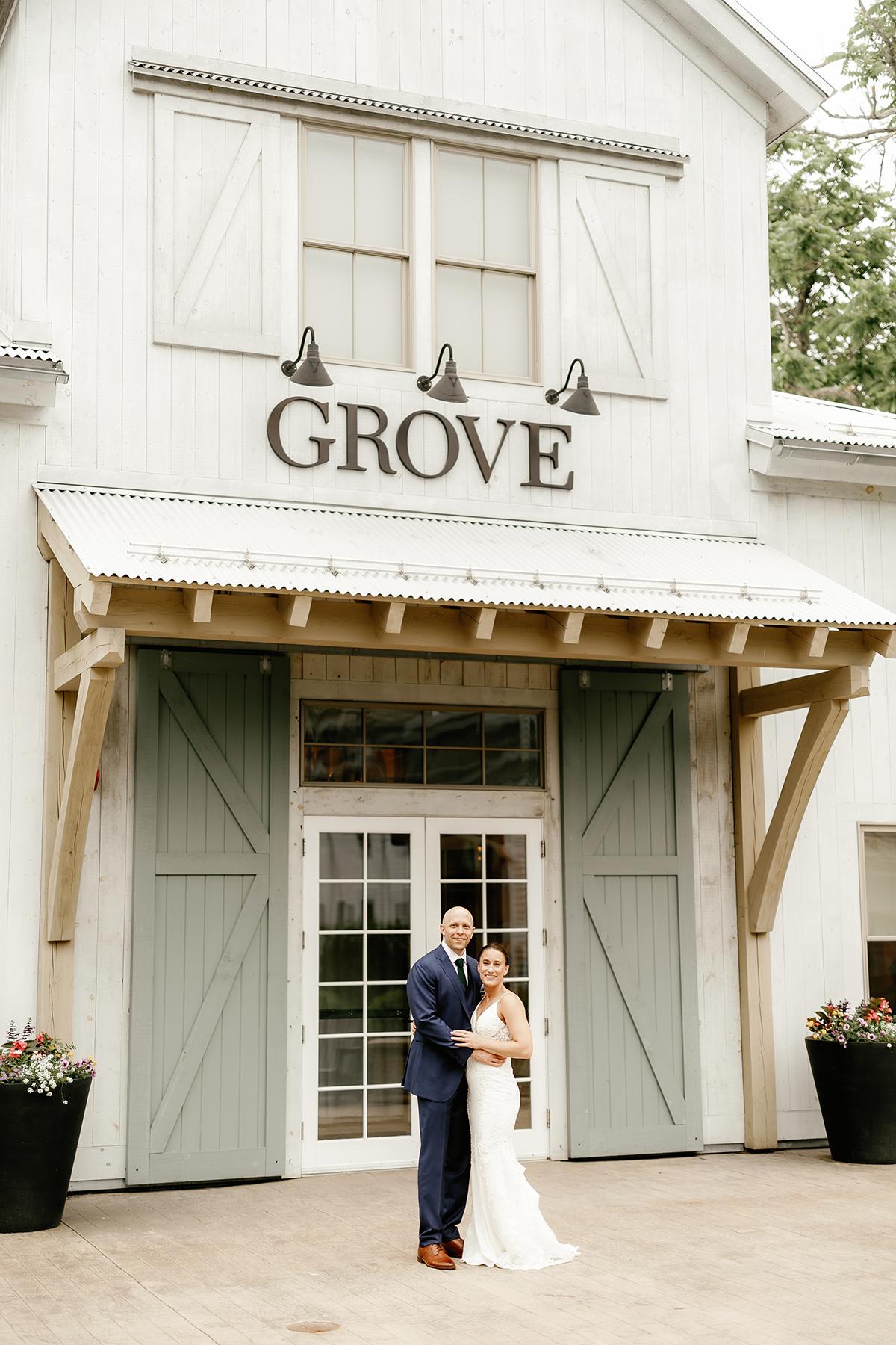 Couple posing in front of a rustic building labeled "Grove."