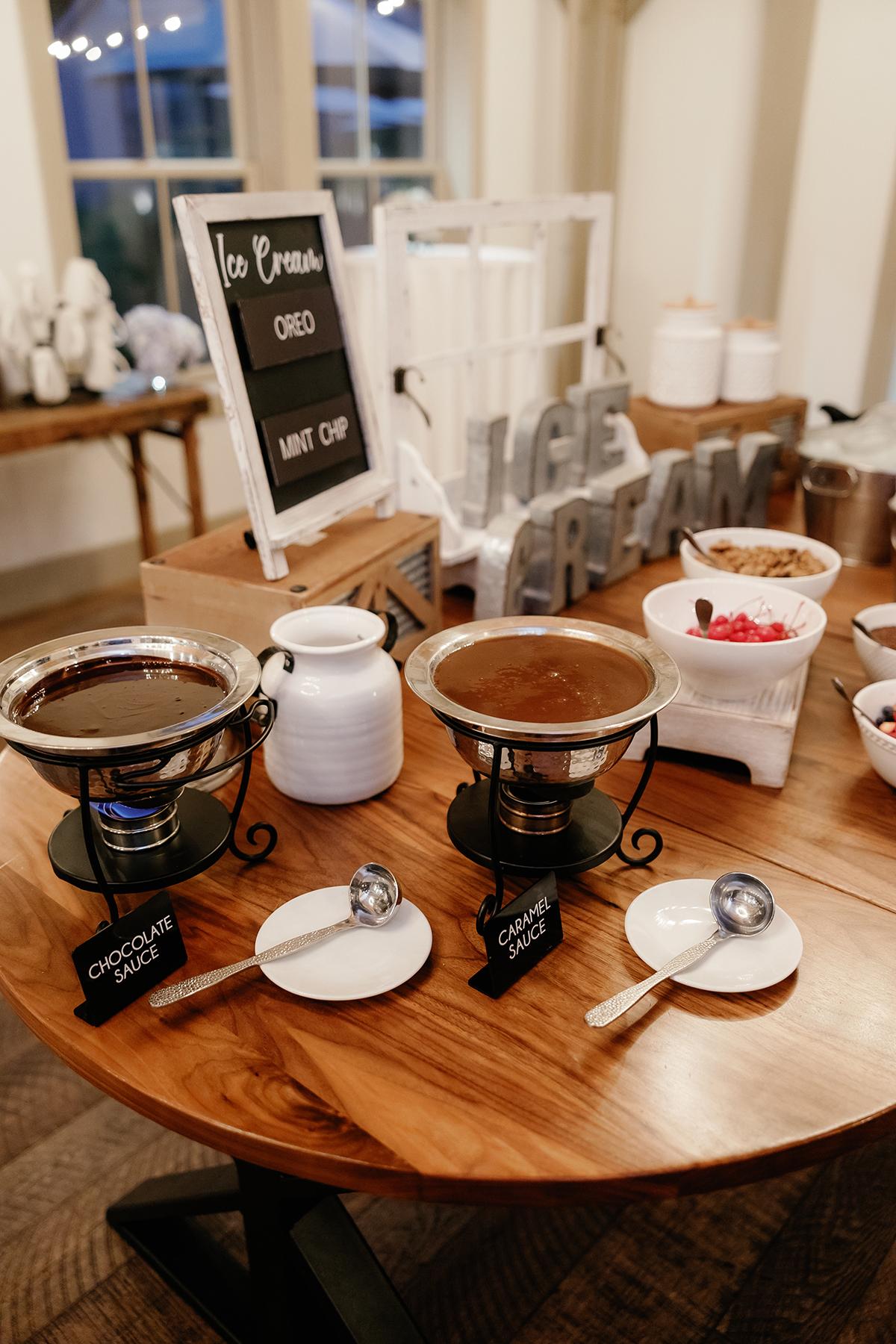 Ice cream dessert station with toppings and sauces on a wooden table.