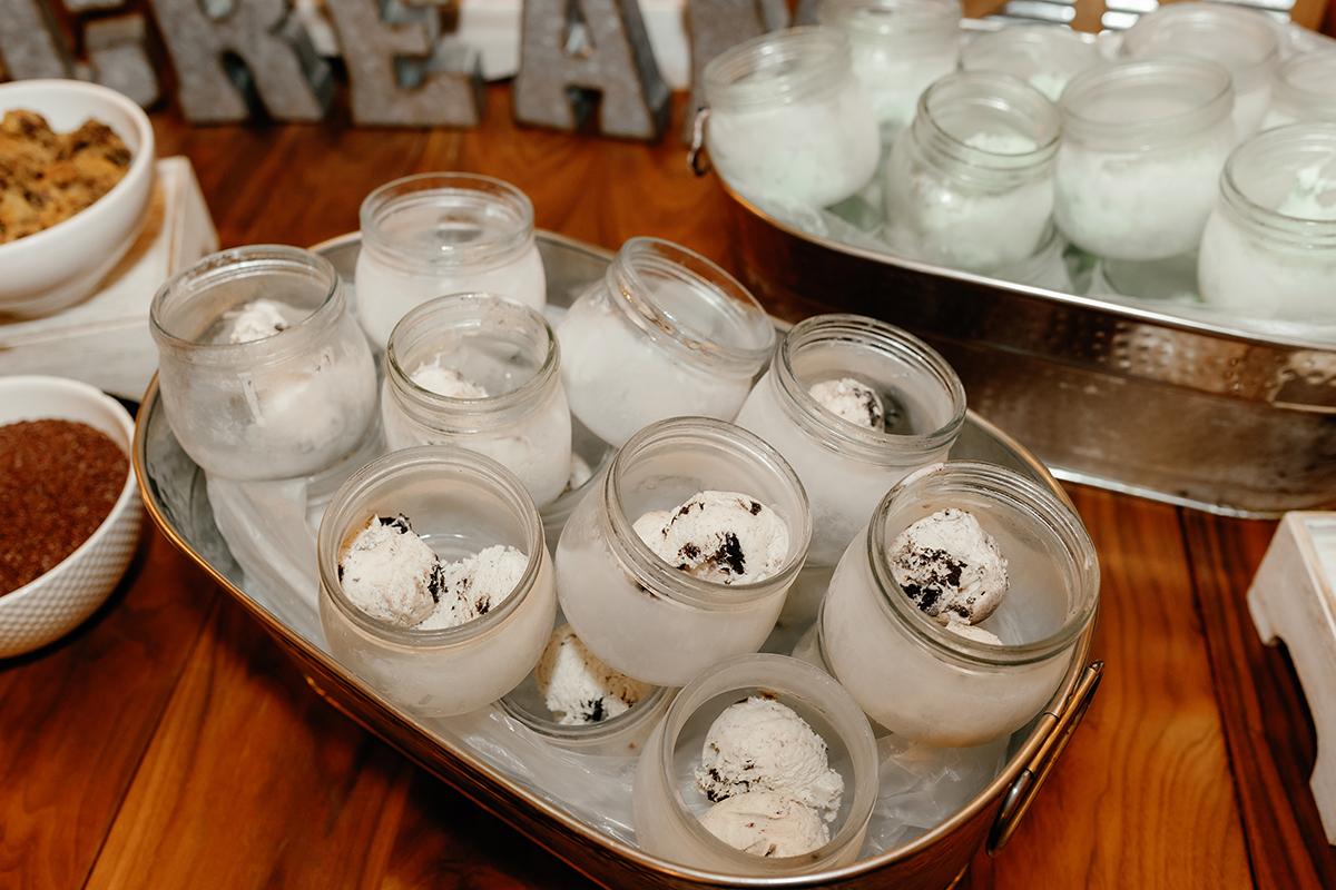 Jars of vanilla ice cream with cookies on a tray with bowls of toppings nearby.
