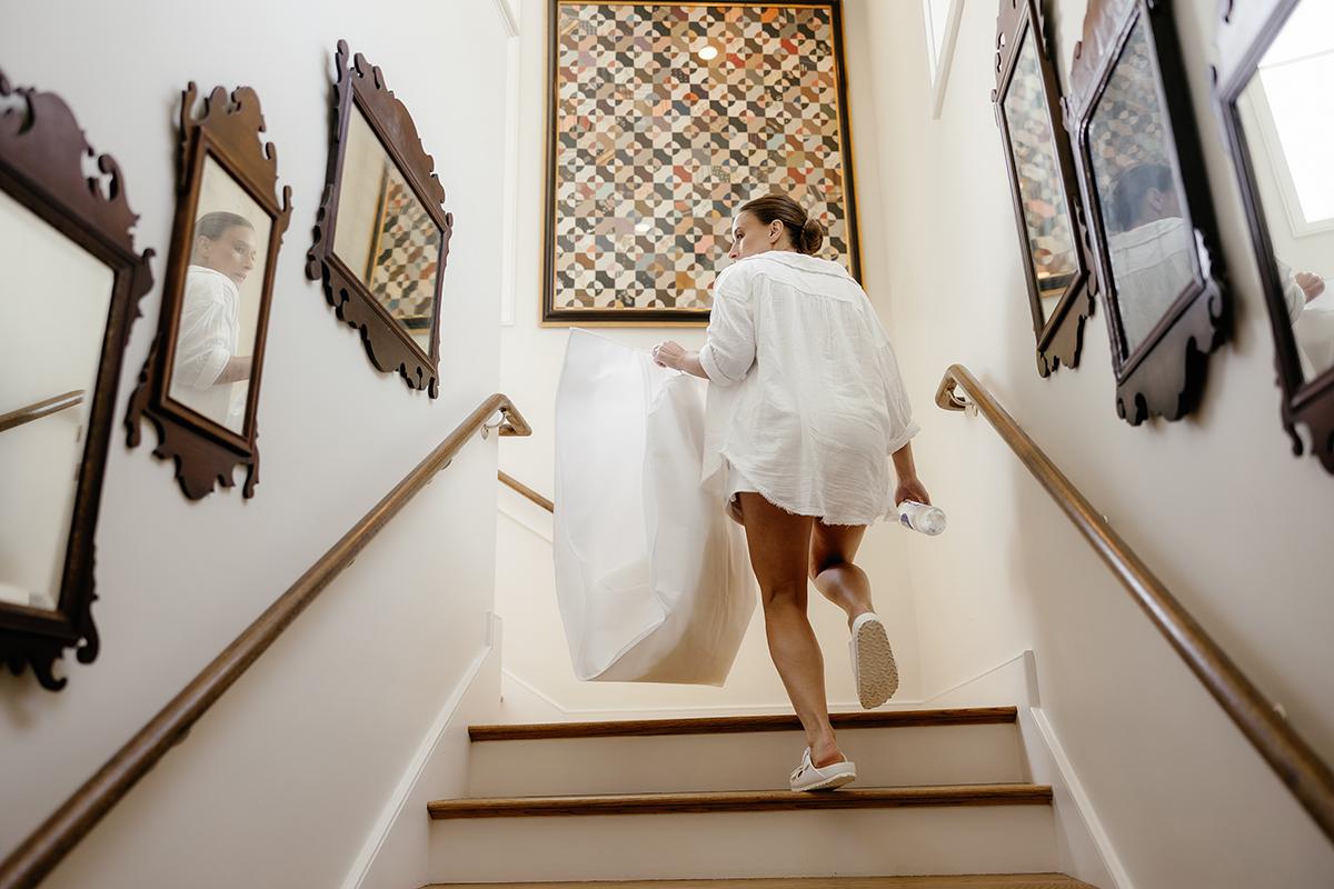 A woman in a white shirt walks up stairs, holding a garment bag.