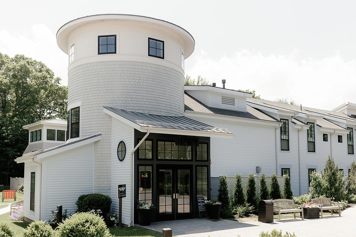 White modern house with a round tower and large windows, surrounded by greenery.