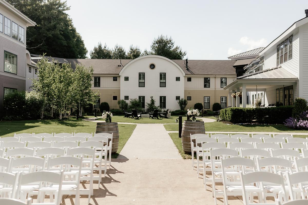 Outdoor wedding venue with white chairs facing a large building.