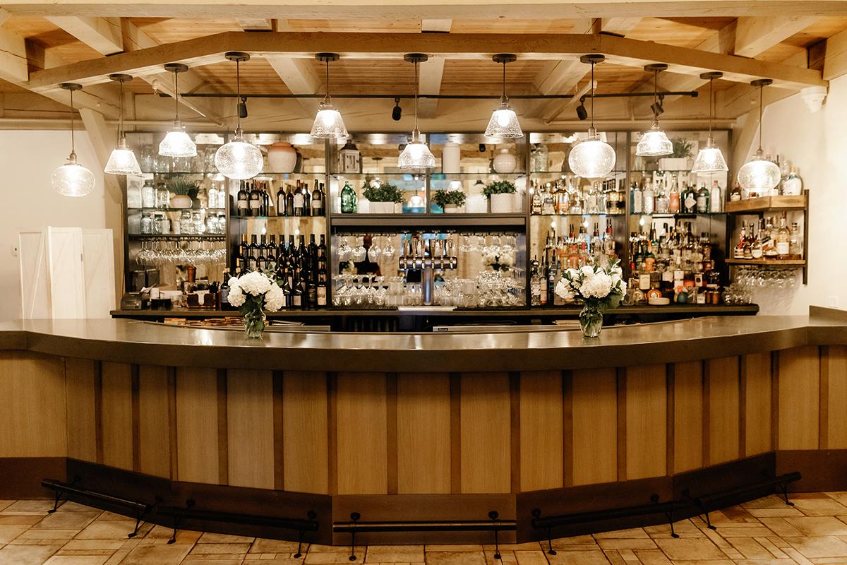 Cozy bar interior with wooden decor, shelves of bottles, and hanging lights.