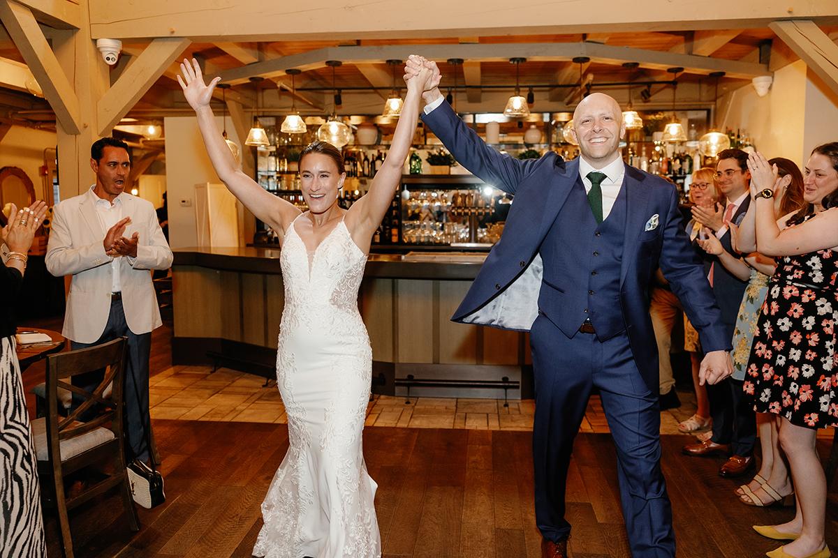 Bride and groom celebrating at a wedding reception with raised arms.