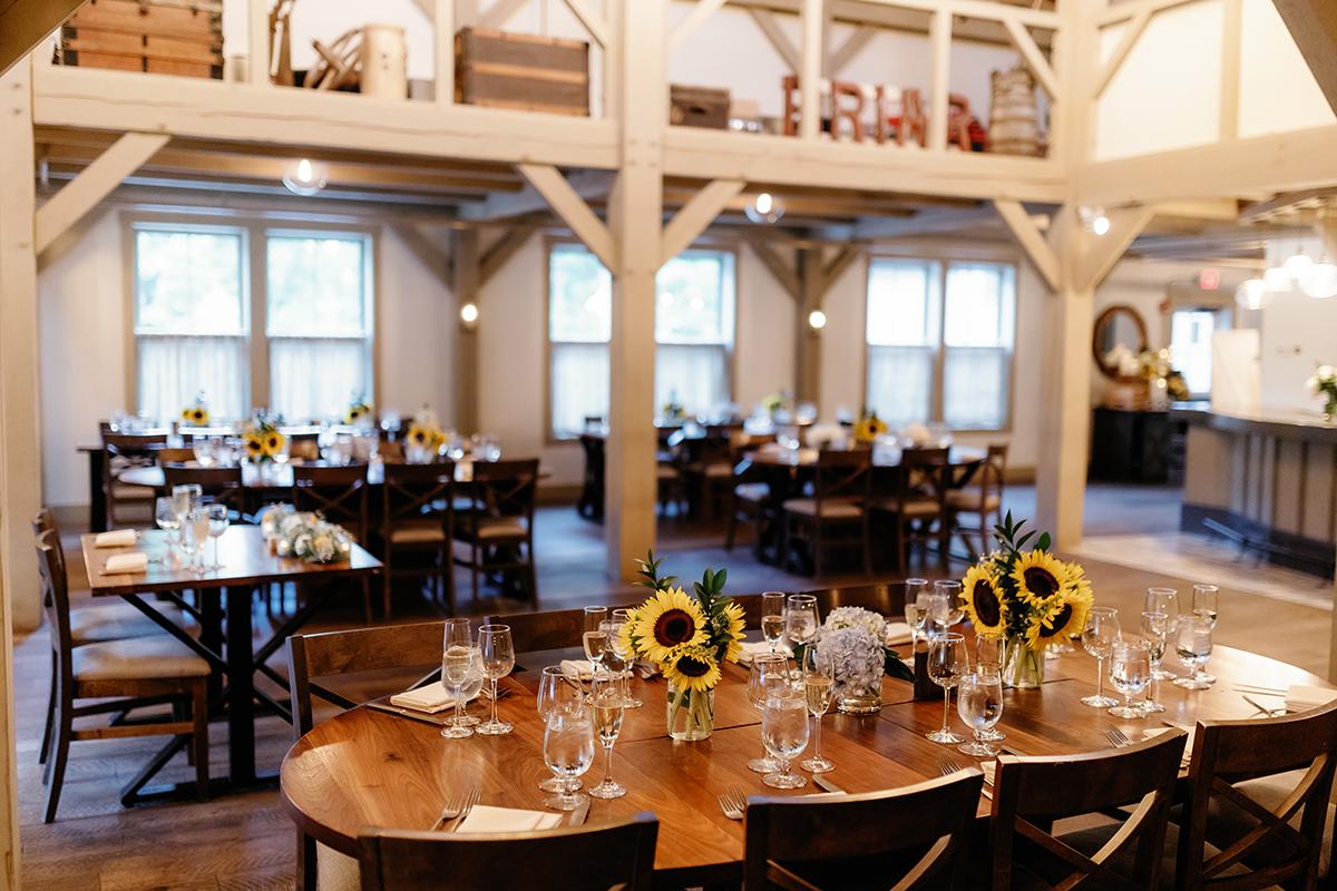 Rustic dining area with wooden tables, sunflower centerpieces, and soft lighting.
