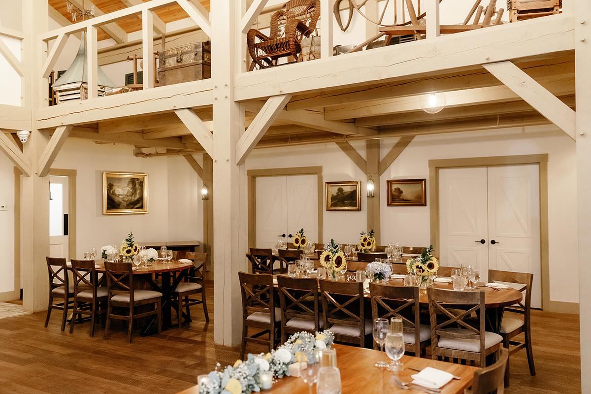 Rustic dining room with wooden tables, sunflower centerpieces, and framed paintings.