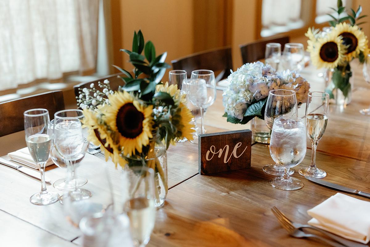 Sunflowers and hydrangeas in vases on a wooden table set for a meal.
