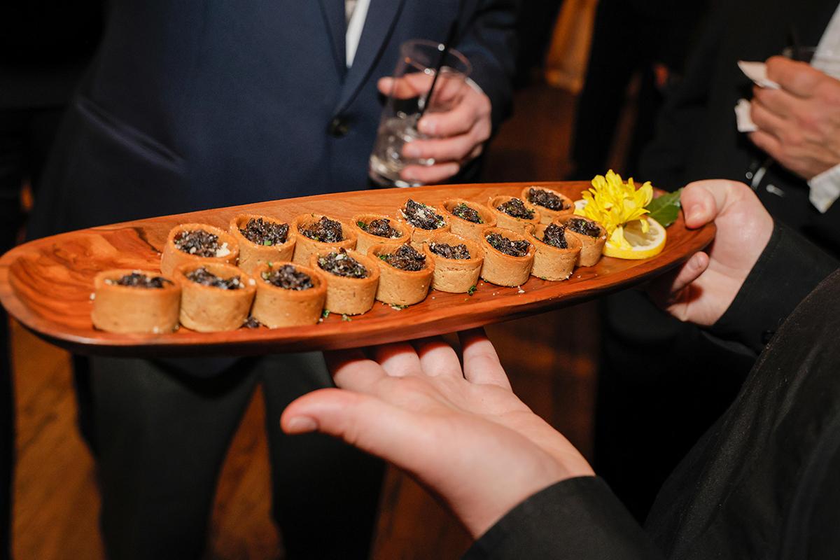 Appetizers on a wooden platter with a lemon slice and yellow flower garnish.