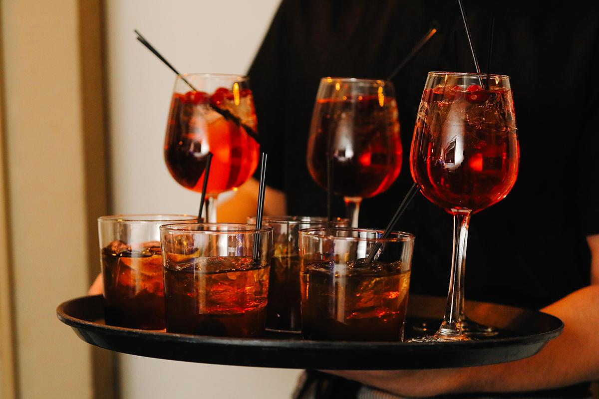 Tray with glasses of red and amber cocktails, garnished with cherries.