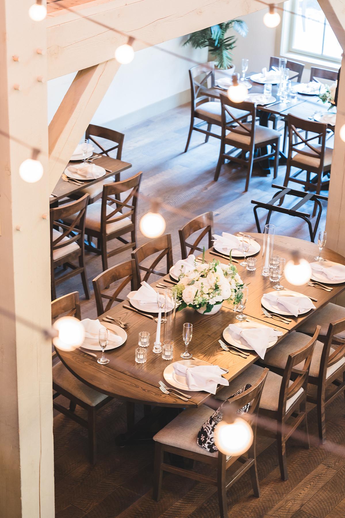 Rustic dining table set with plates, candles, and flowers, under warm string lights.