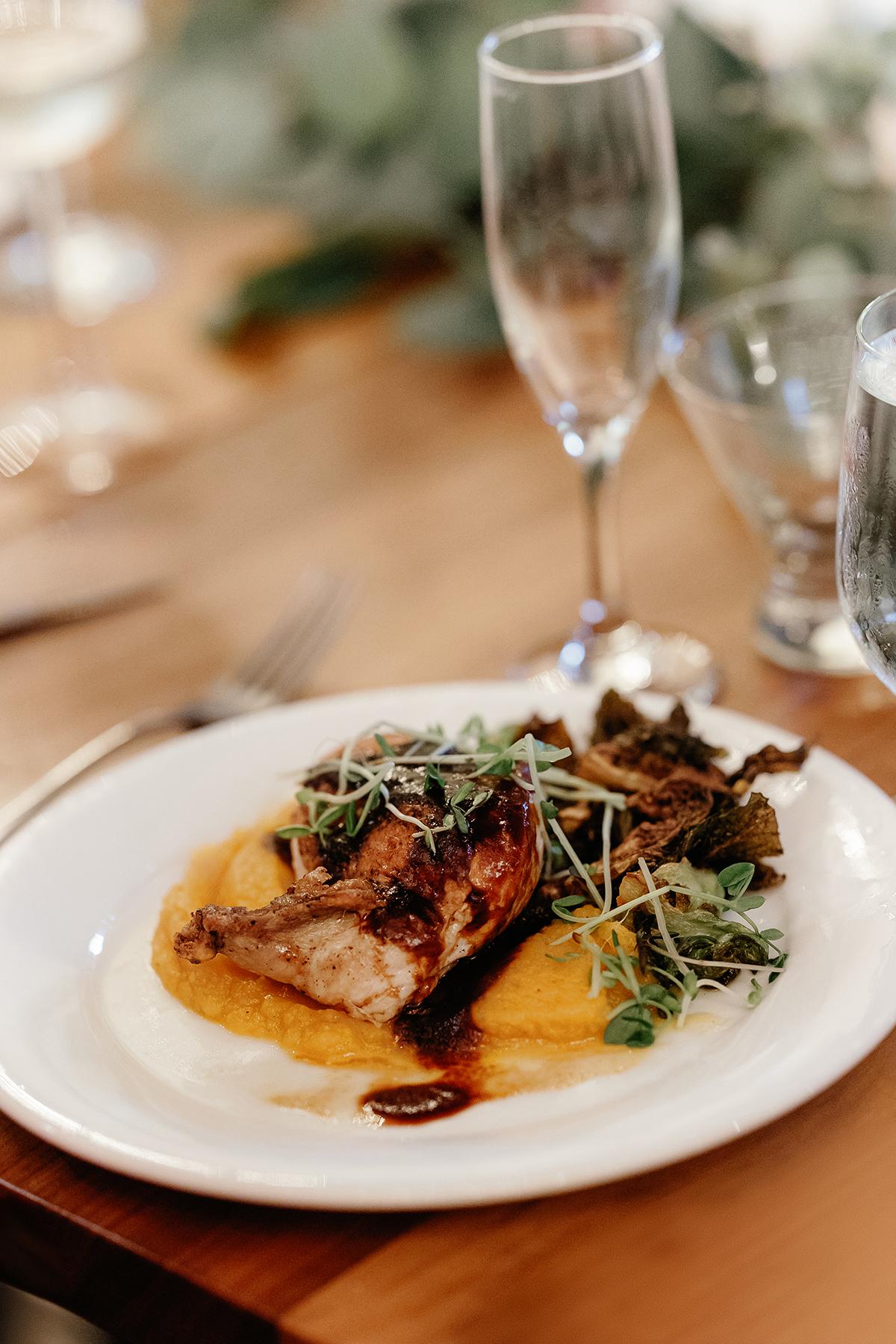 Grilled chicken on puree with greens, served on a white plate beside a champagne glass.