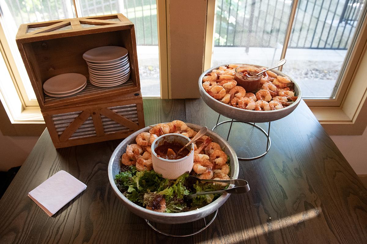 Shrimp cocktail platters on a table by a window with plates and a napkin nearby.
