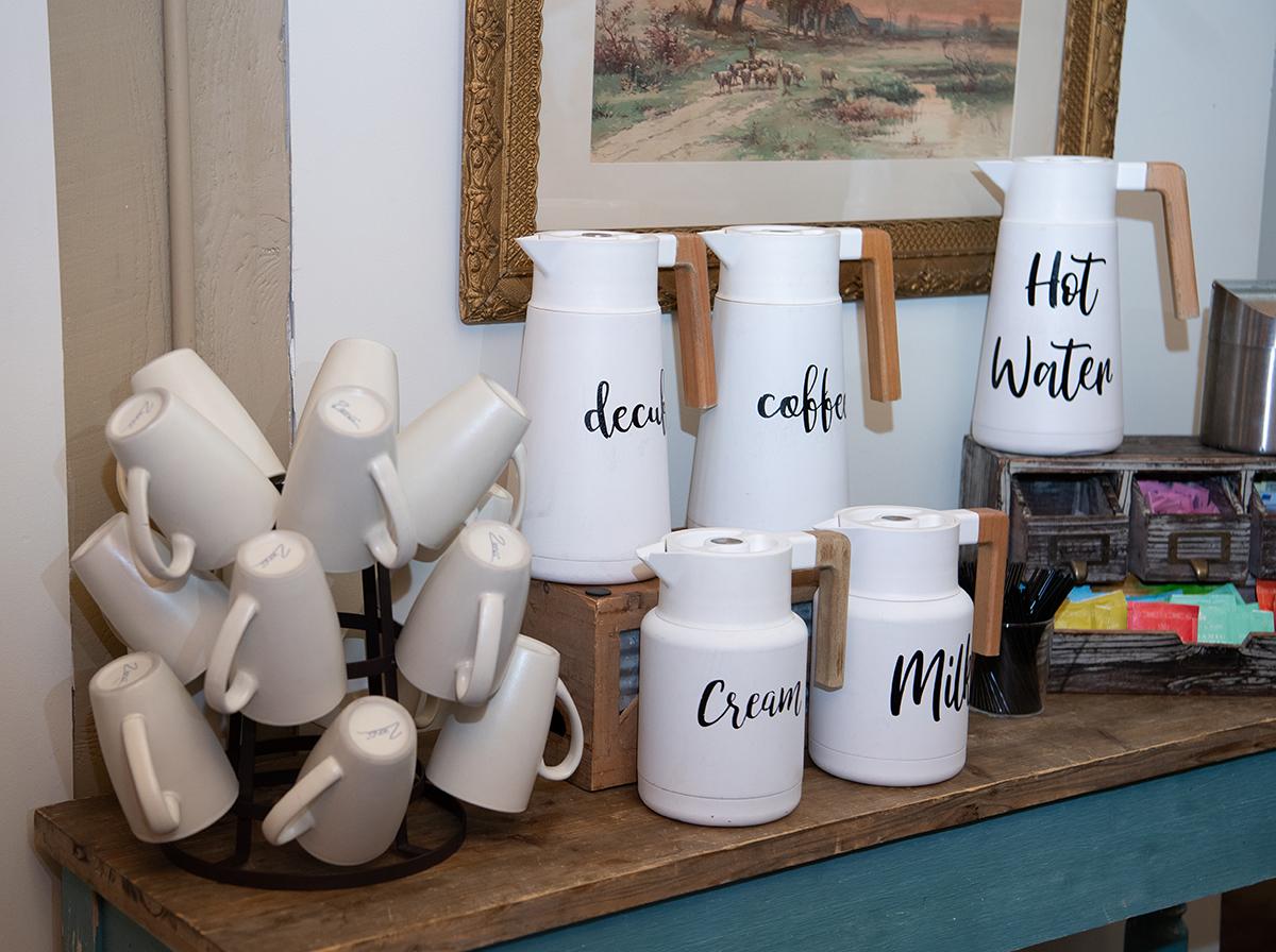 White drink dispensers and cups on a wooden table.