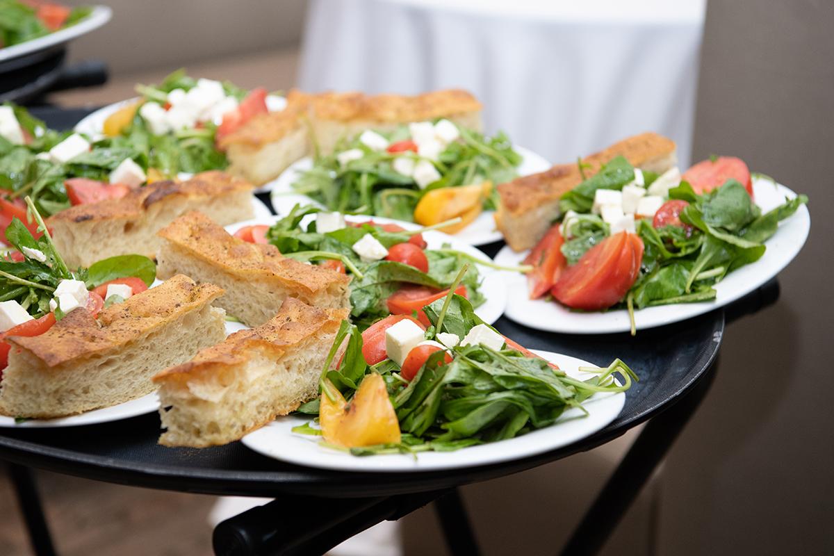 Salad plates with arugula, tomatoes, feta, and focaccia slices on a table.