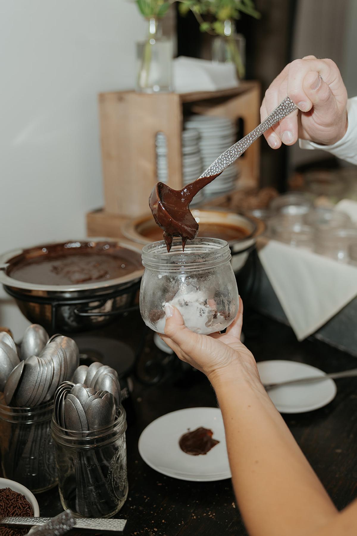 Hand pouring chocolate sauce into a jar near dining setup.
