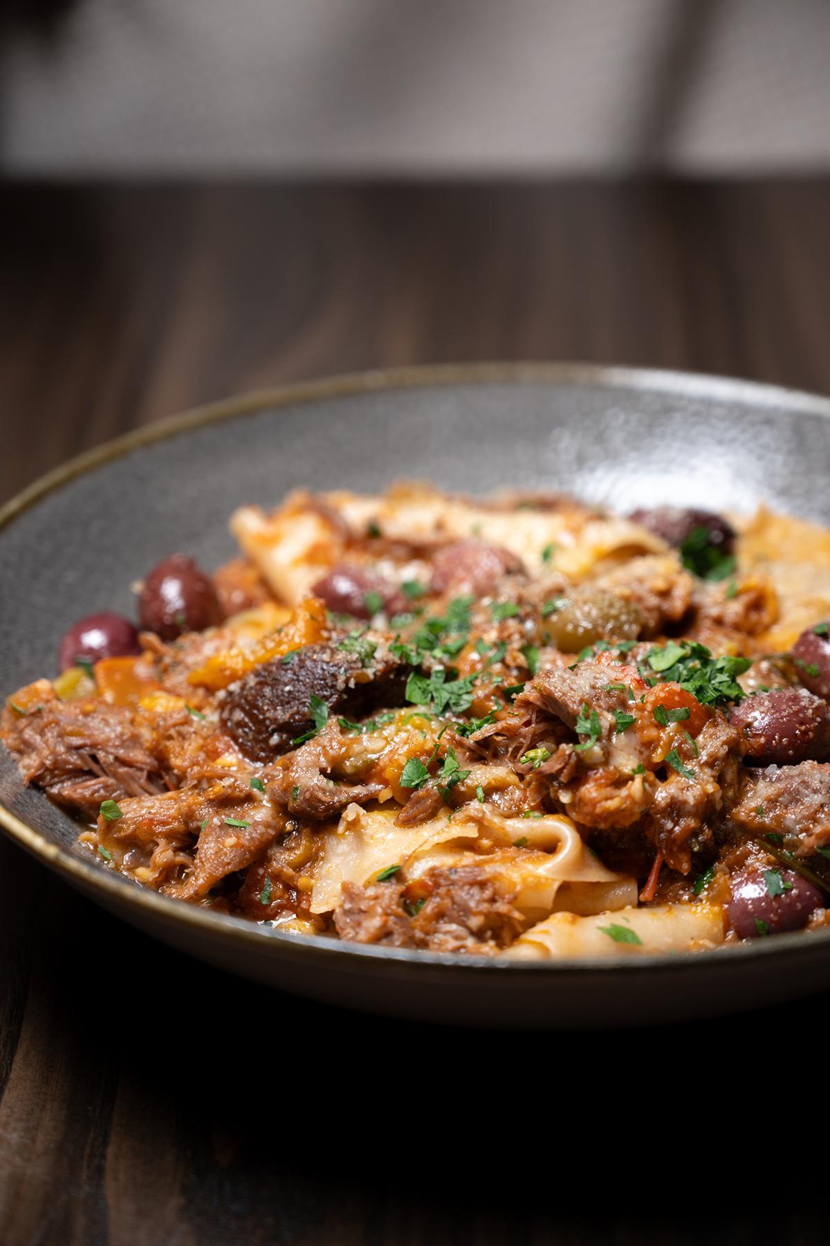 Pasta dish with beef, olives, and parsley in a dark bowl.