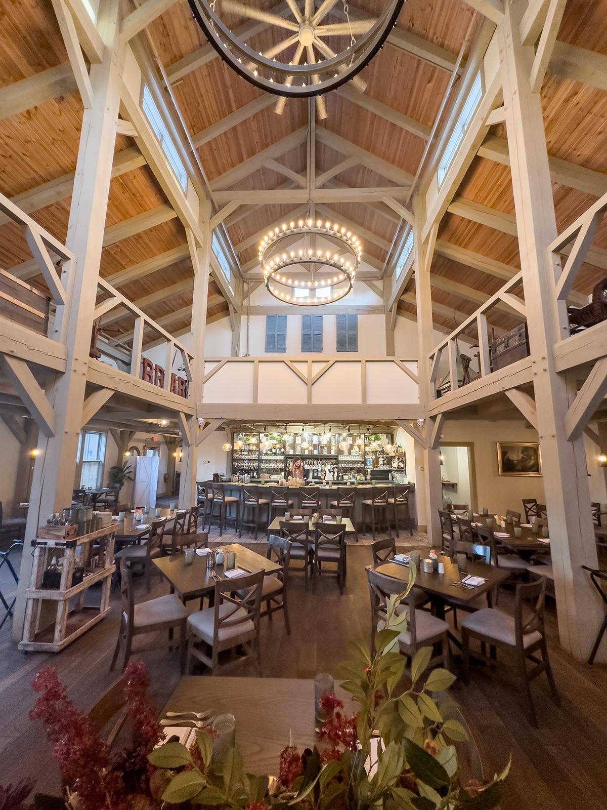 Rustic restaurant interior with high ceiling and wooden beams. Tables set for dining.