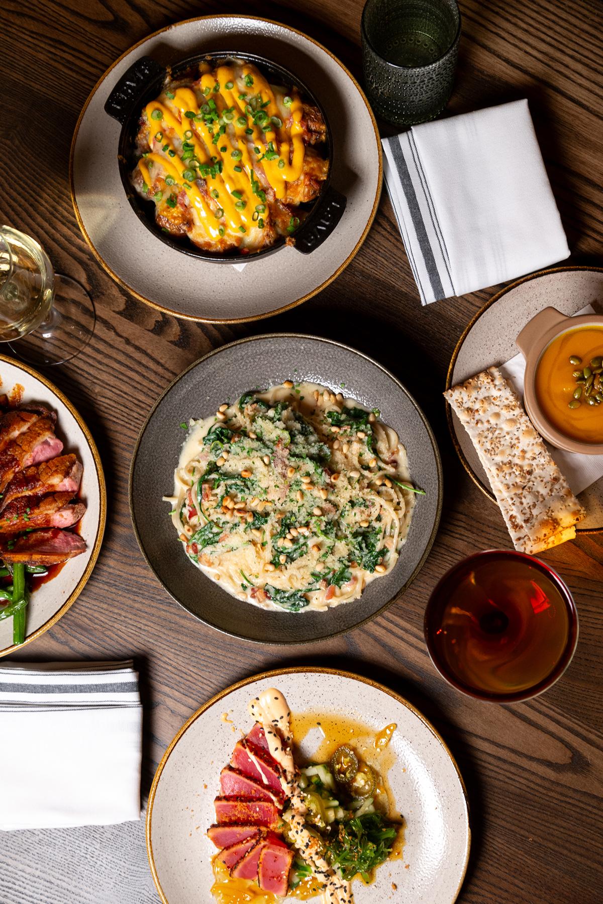 Assorted gourmet dishes on a wooden table, including pasta and sliced meat.