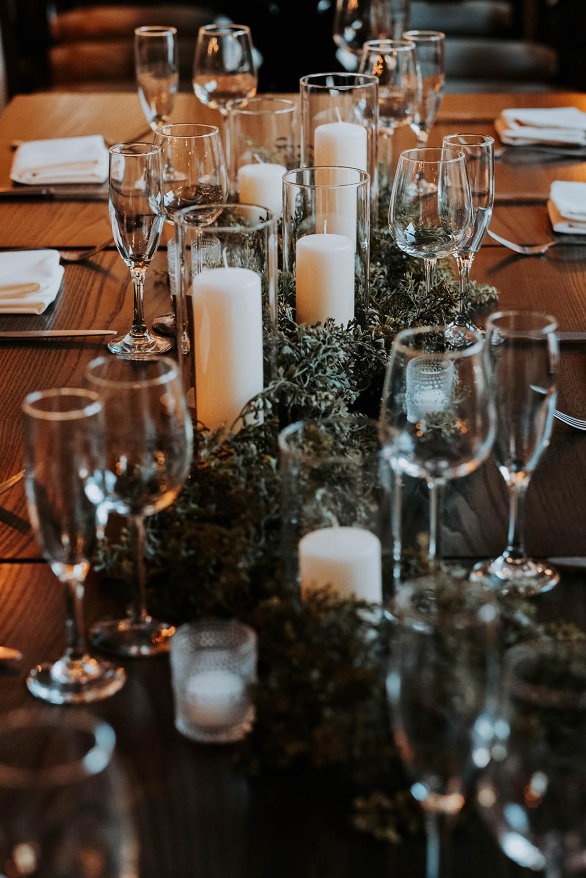 Candlelit dining table set with glassware and greenery.