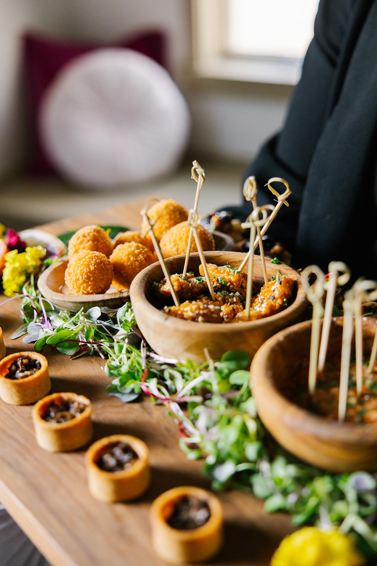 Assorted appetizers in wooden bowls with skewers on a table, garnished with fresh greens.