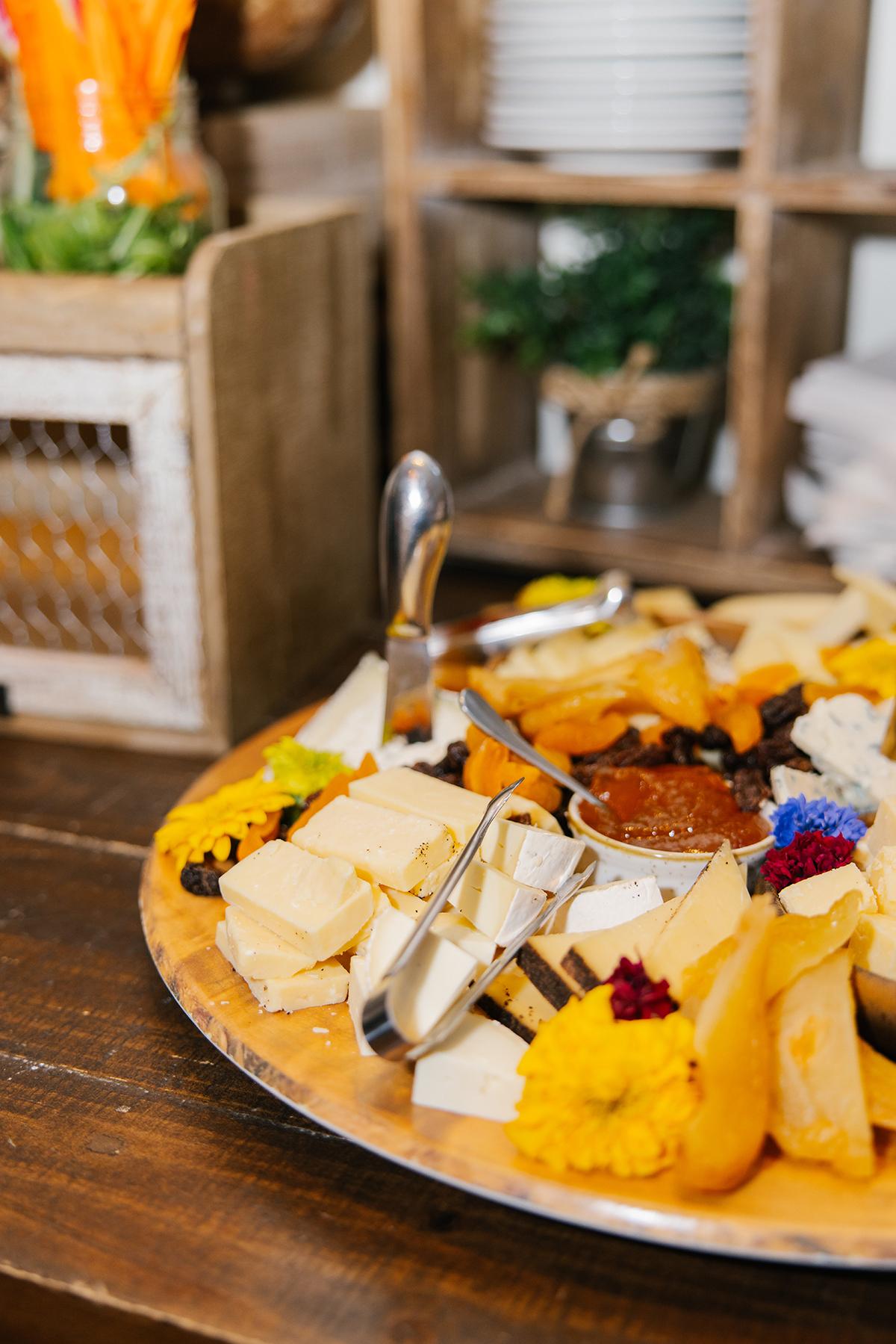 Cheese platter with various cheeses, fruits, and garnishes on a wooden table.