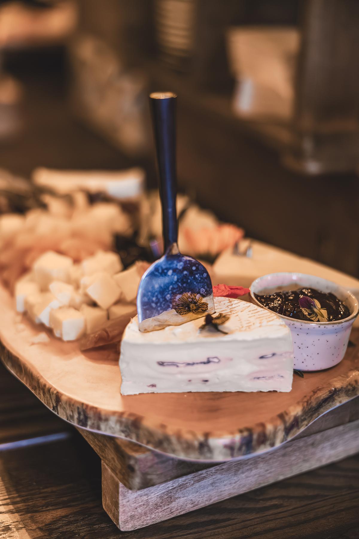 Cheese board with various cheeses and a small bowl of jam.
