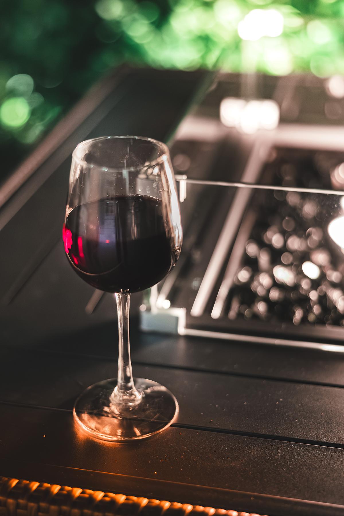 Glass of red wine on a table with a fire pit, soft lighting.