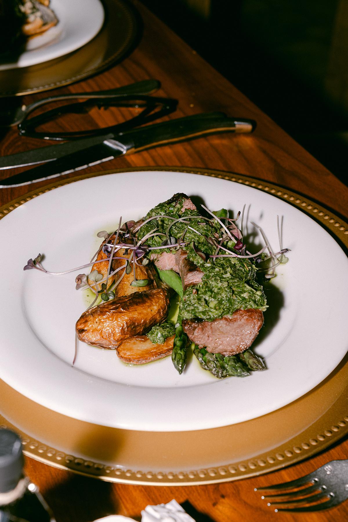 Grilled meat with roasted potatoes and greens on a white plate.