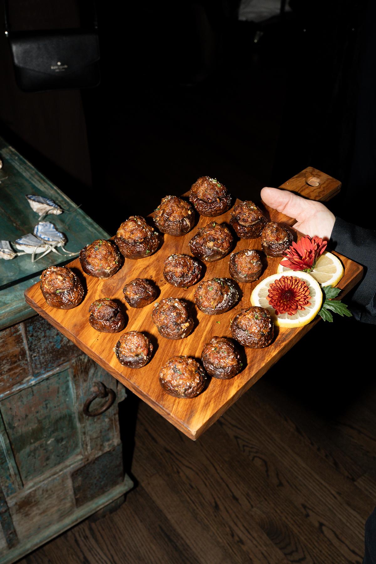 A person holding a wooden tray of small, round pastries with figs.