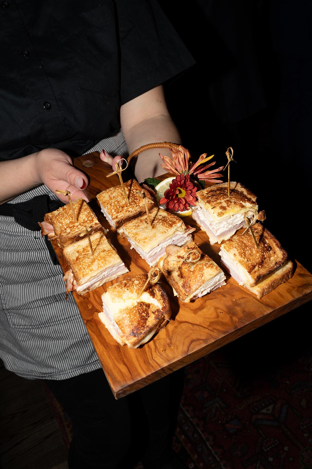 Tray of sandwiches held by a person, garnished with flowers.