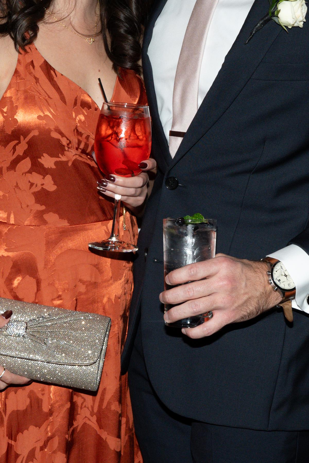 Elegant couple holding drinks, woman in orange dress, man in dark suit.