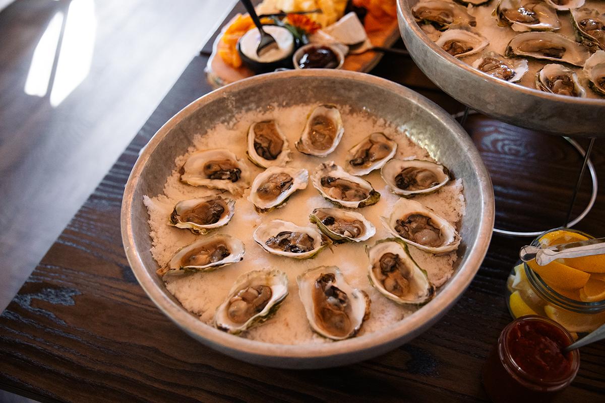 Oysters on ice in a metal bowl on a wooden table.