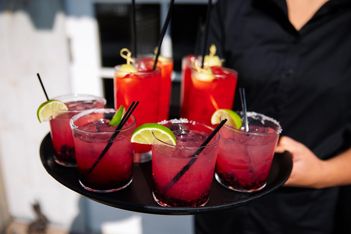 Server carries tray of red cocktails with lime and straws.