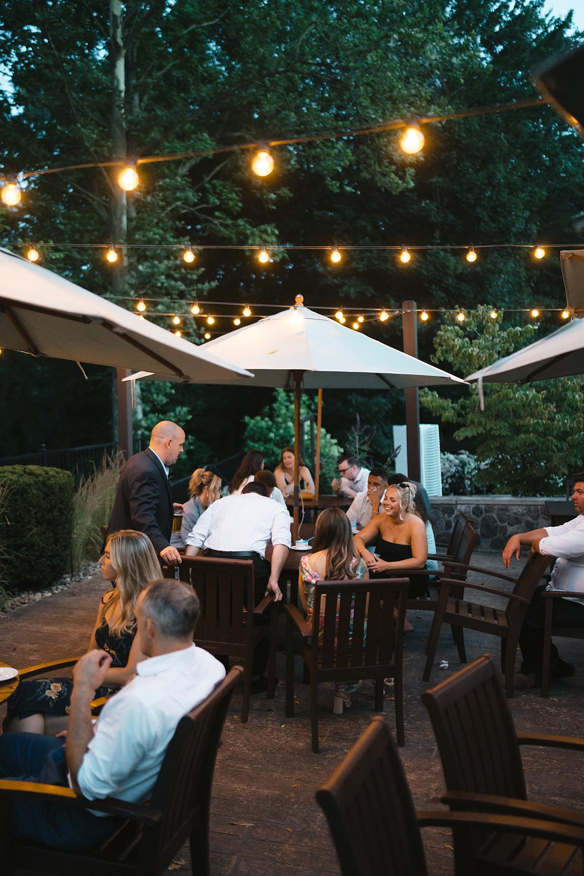 Outdoor restaurant seating with people under string lights and umbrellas.