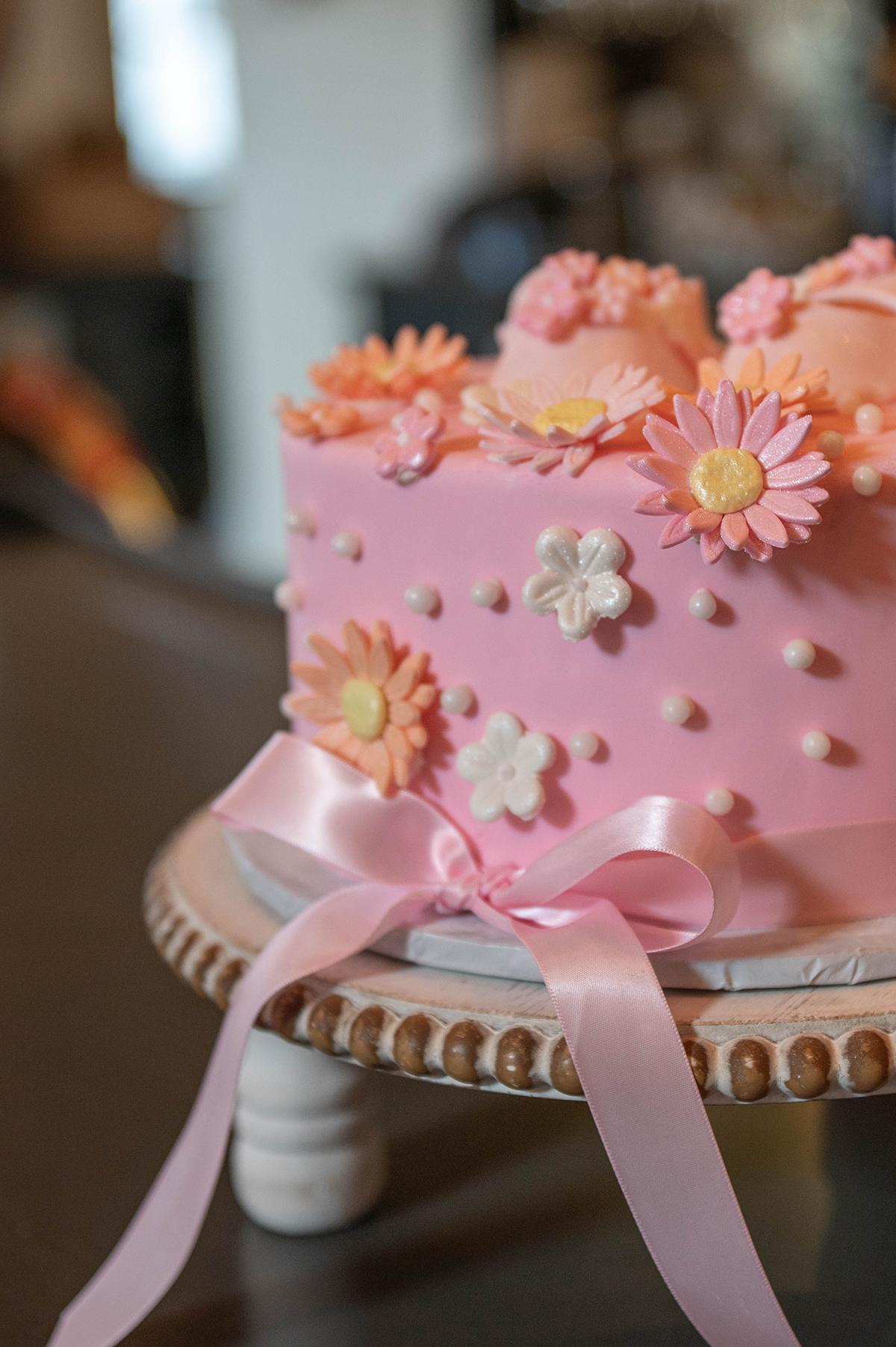 Pink cake with fondant flowers and ribbon on a cake stand.
