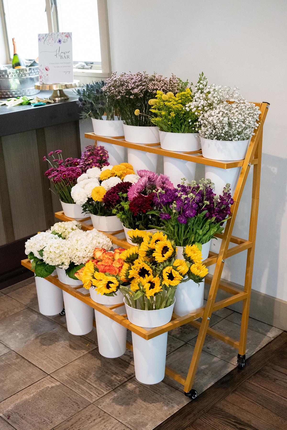 Flowers arranged in white pots on a wooden rack, indoors.