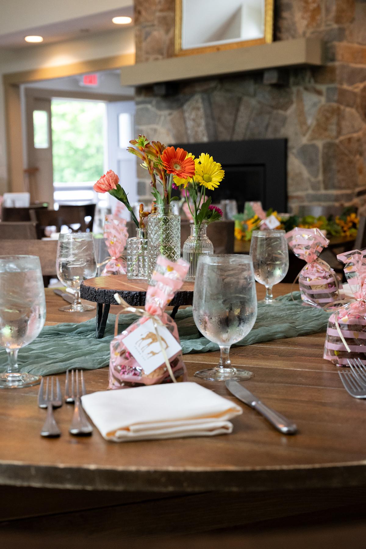Elegant dining table set with flowers, glassware, and stone fireplace backdrop.