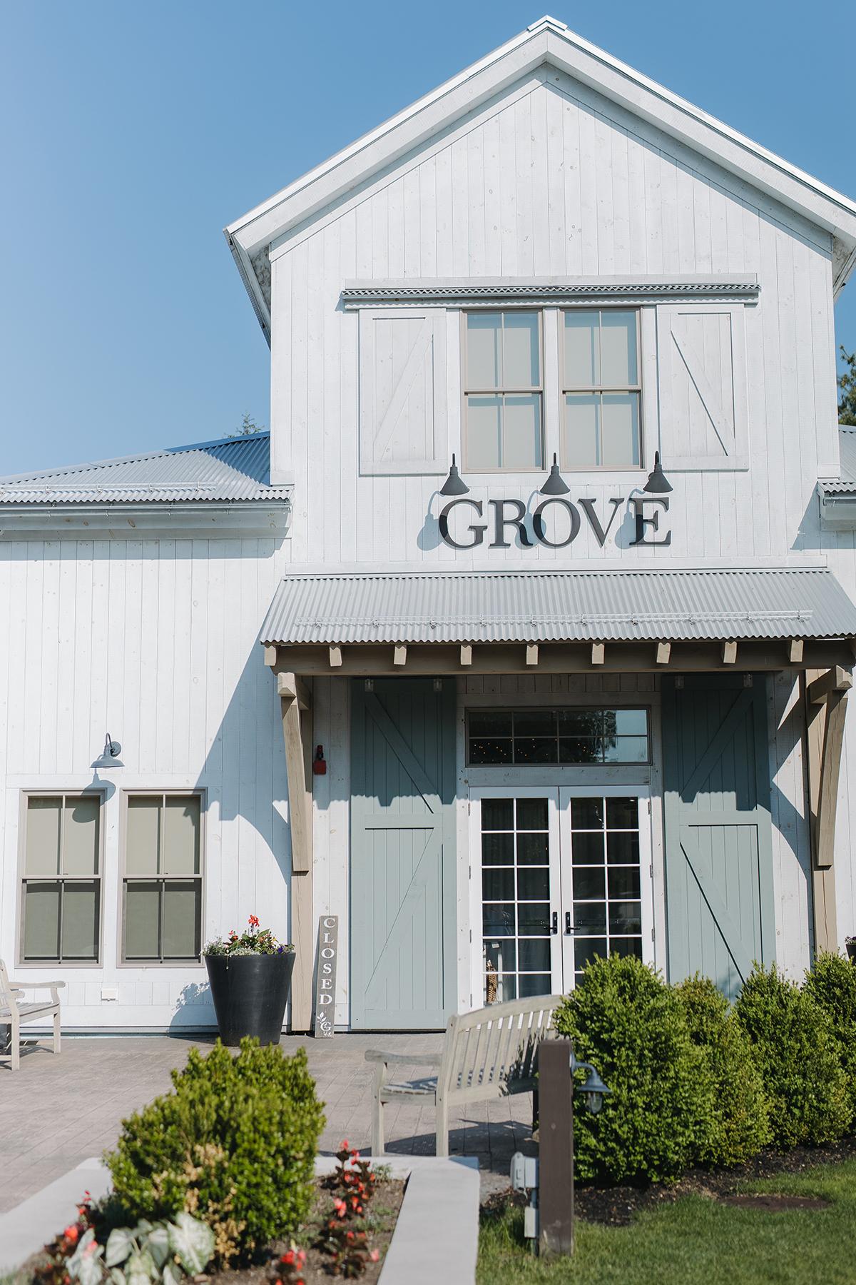 White building with large windows, sign reading "Grove," and greenery in front.