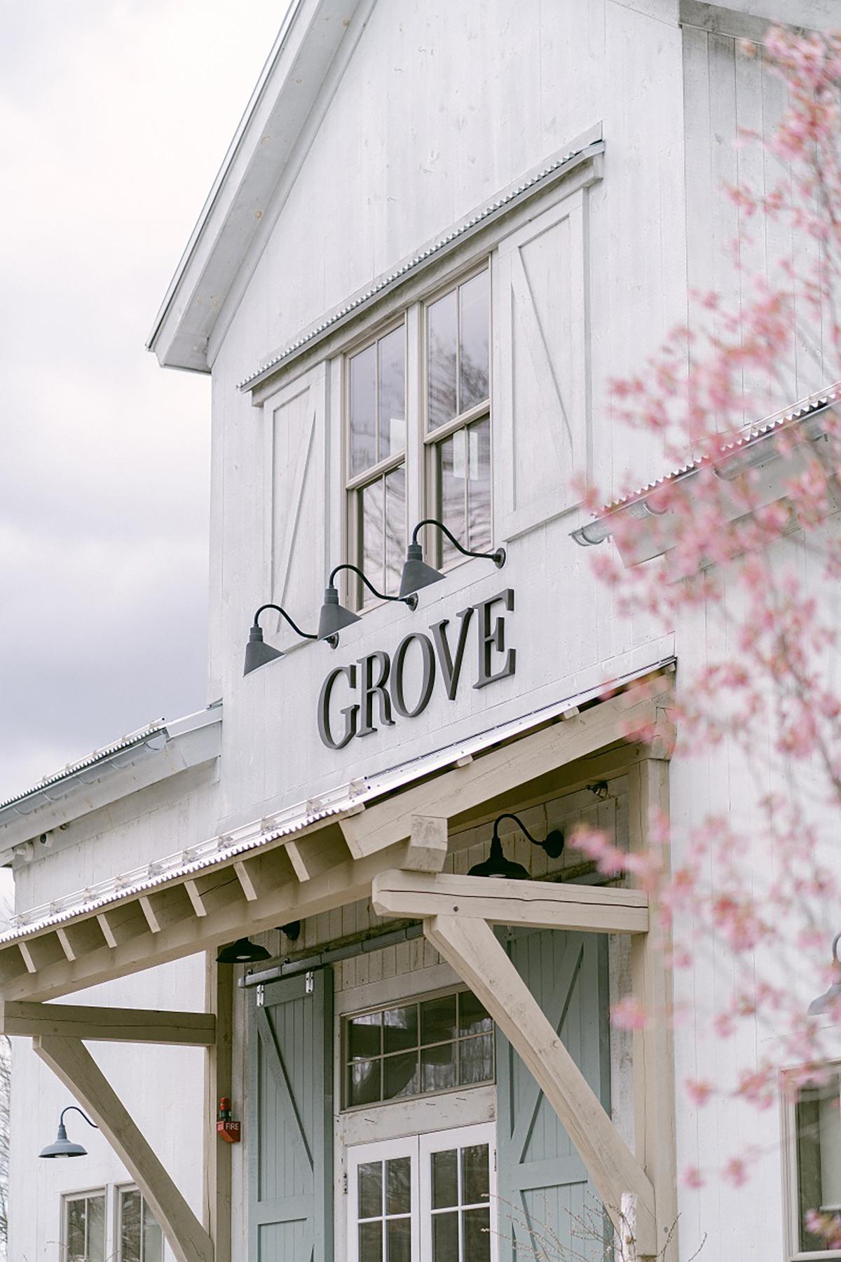 White building with "Grove" sign, light pink blossoms in foreground.